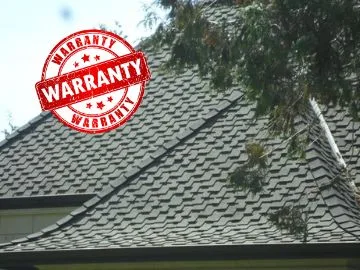 A rooftop covered in dark gray shingles, partially obscured by tree branches, showcases its durability. A bold red Limited Lifetime Warranty stamp overlays the upper left corner of the image, promising long-lasting protection.