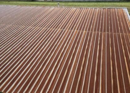 A corrugated metal roof in Richmond, possibly a candidate for metal roof conversion or torch-on metal roof installation, shows visible rust and white streaks along each sheet. Grass and part of a fence can be seen in the background.